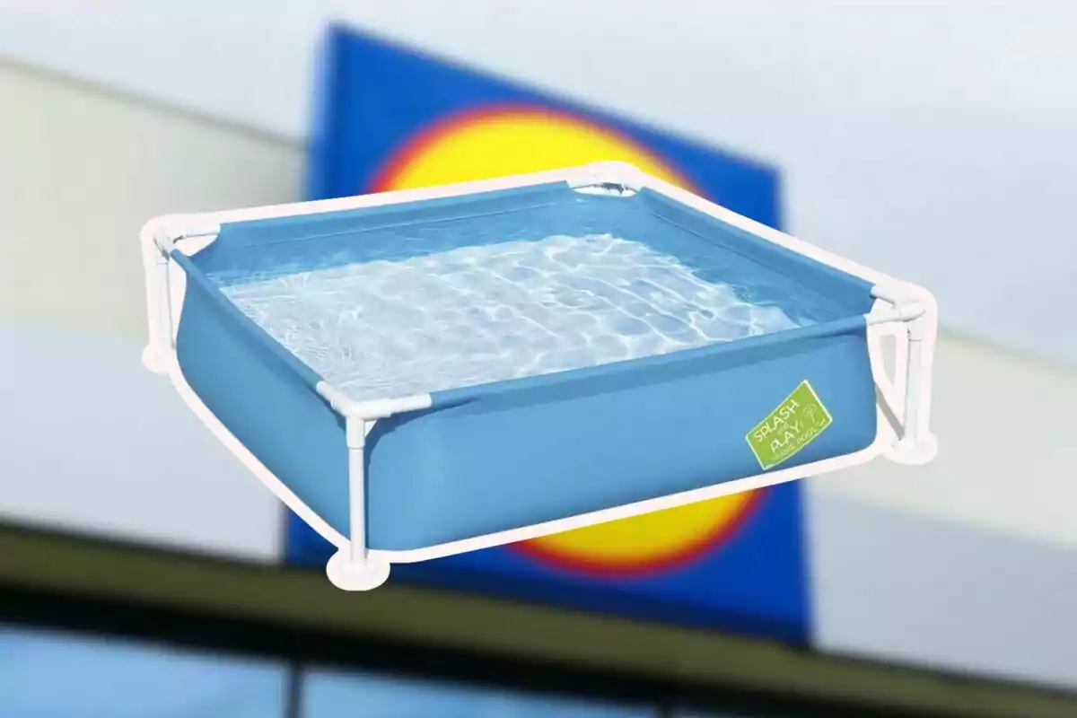 Piscina infantil blava d'estructura quadrada amb aigua sobre un fons desenfocat d'un rètol de supermercat