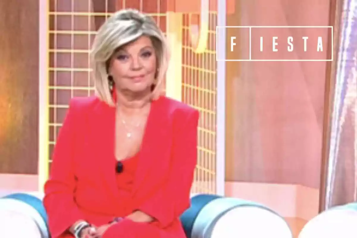 Terelu Campos con traje rojo sentada en un plató de televisión con el logo de Fiesta en el fondo