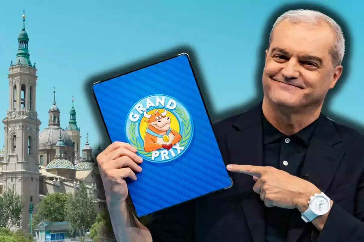 Ramón García sonriente sostiene y señala una carpeta azul con el logo de Grand Prix frente a un fondo con la Basílica del Pilar.