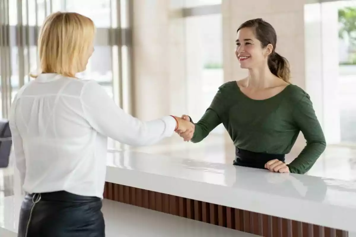 Dos mujeres se saludan con un apretón de manos en una recepción moderna mientras sonríen