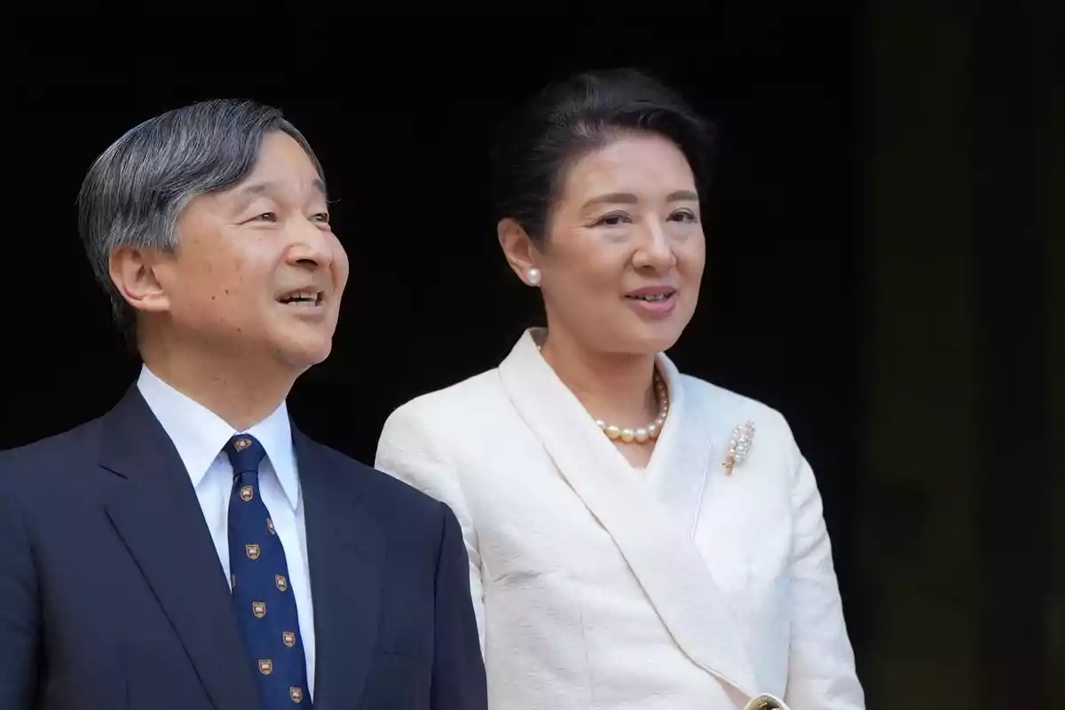 Naruhito y Masako elegantemente vestidos posan juntos y sonríen frente a un fondo oscuro. Naruhito y Masako elegantemente vestidos posan juntos y sonríen frente a un fondo oscuro.