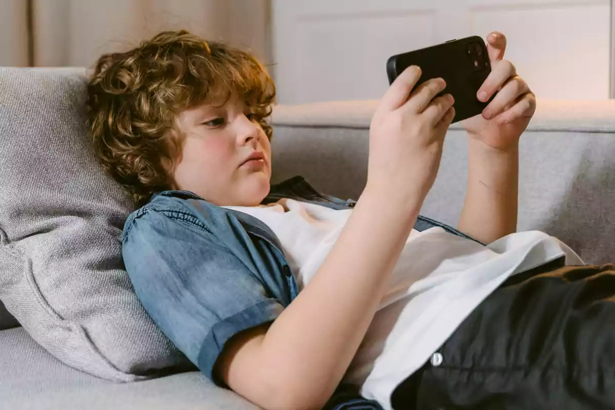 Child lying on a couch using a mobile phone Child lying on a couch using a mobile phone