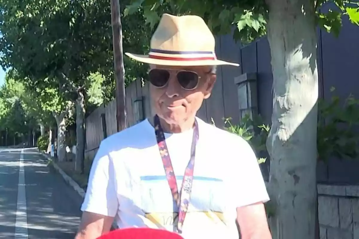 Pla mitjà de José Ortega Cano amb barret d’ala ampla i ulleres de sol caminant per un carrer arbrat en un dia assolellat. Pla mitjà de José Ortega Cano amb barret d’ala ampla i ulleres de sol caminant per un carrer arbrat en un dia assolellat.