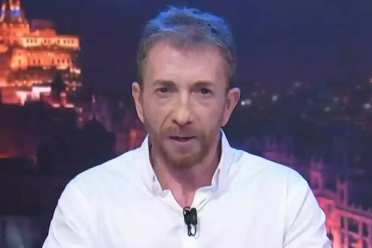 Pablo Motos de cabello corto y barba rojiza vistiendo camisa blanca frente a un fondo urbano iluminado por la noche en El Hormiguero Pablo Motos de cabello corto y barba rojiza vistiendo camisa blanca frente a un fondo urbano iluminado por la noche en El Hormiguero