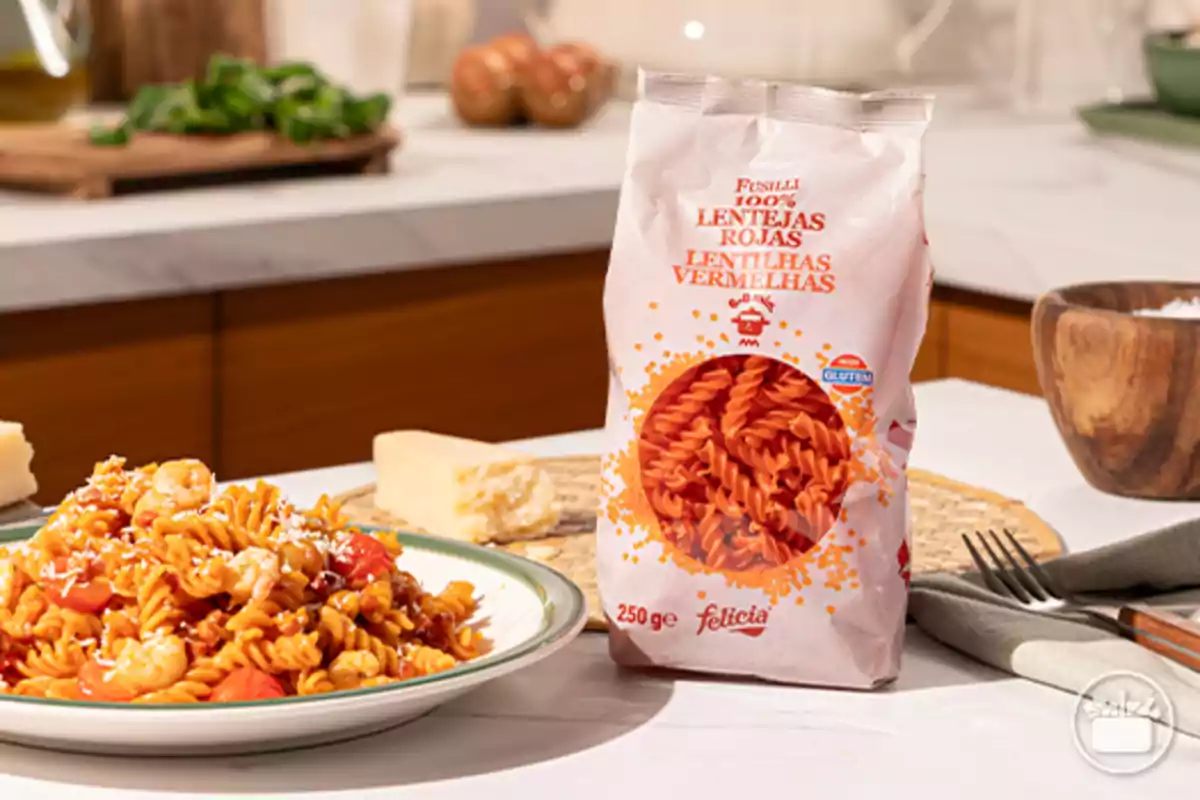 Paquet de fusilli de llenties vermelles al costat d’un plat de pasta bullida amb gambes i formatge ratllat en una cuina moderna Paquet de fusilli de llenties vermelles al costat d’un plat de pasta bullida amb gambes i formatge ratllat en una cuina moderna