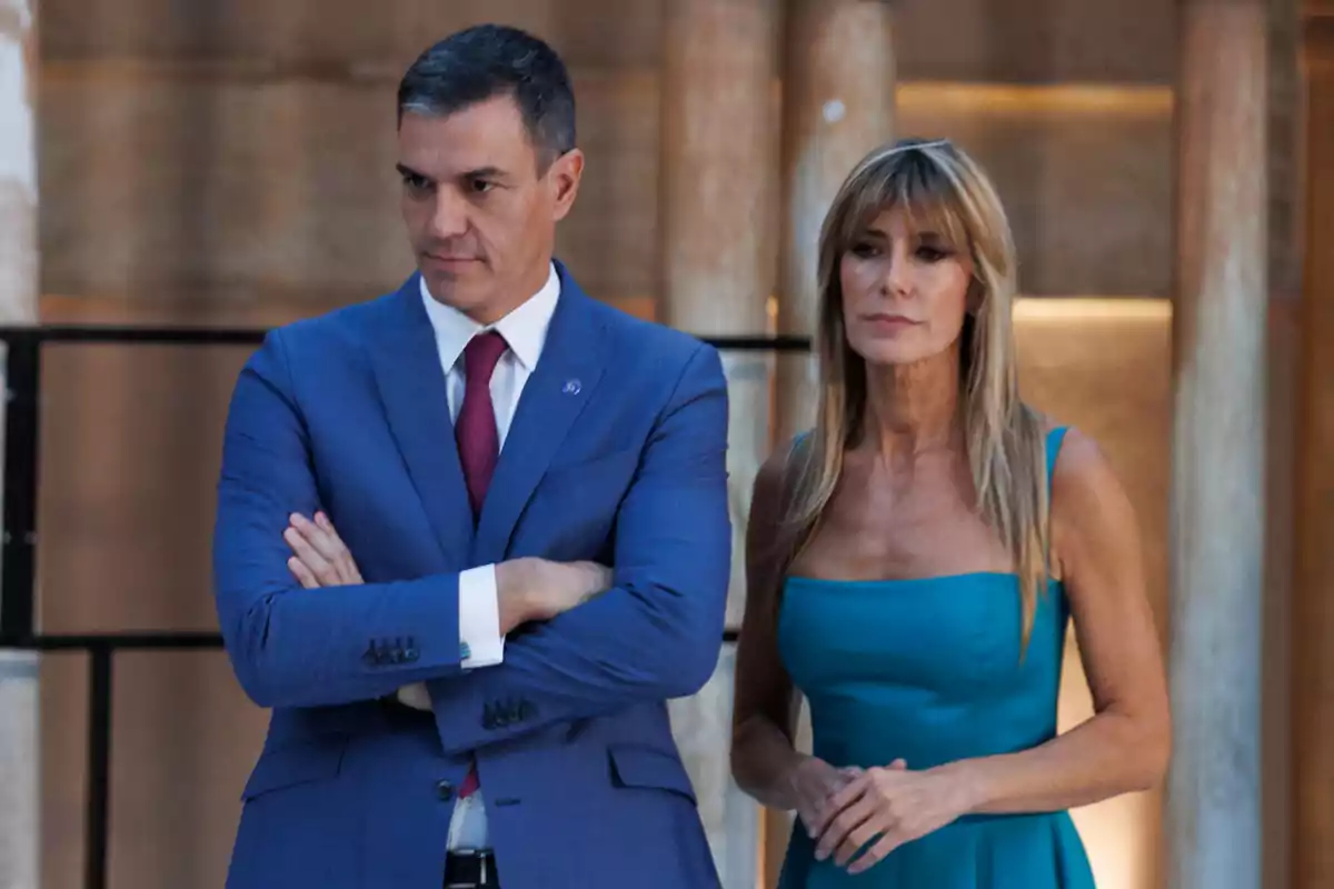Pedro Sánchez amb vestit blau i corbata vermella està dret al costat de Begoña Gómez amb vestit blau turquesa en un entorn elegant amb columnes de fons