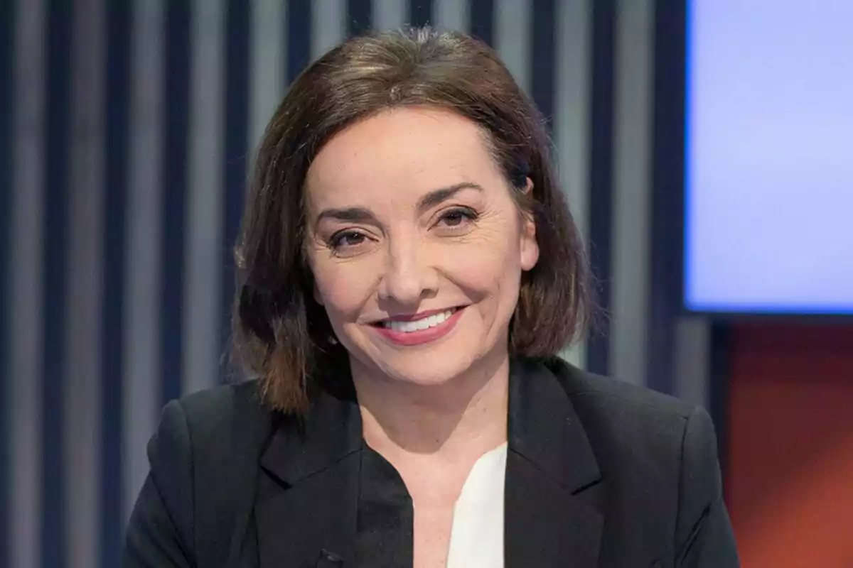 Pepa Bueno de cabello corto y oscuro con saco negro y blusa blanca sonriendo frente a un fondo con líneas verticales. Pepa Bueno de cabello corto y oscuro con saco negro y blusa blanca sonriendo frente a un fondo con líneas verticales.