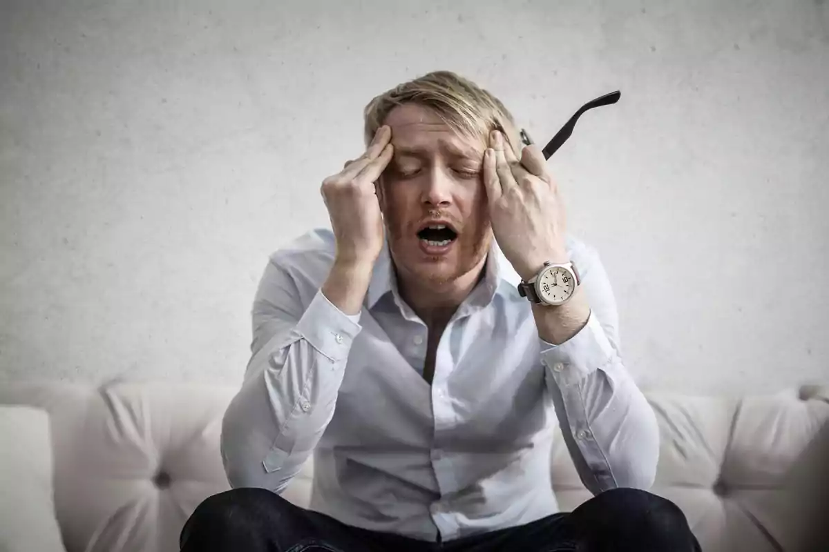Hombre sentado en un sofá con expresión de estrés y las manos en la cabeza