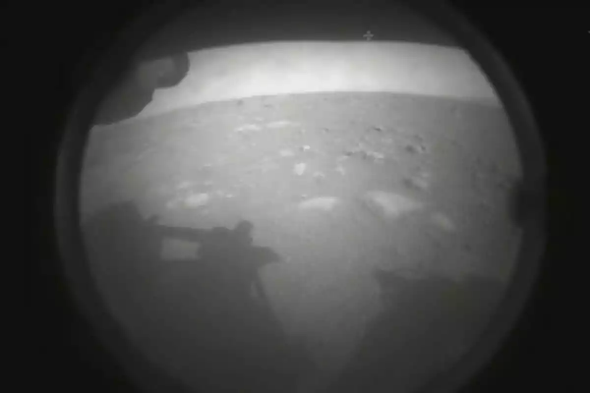 Imagen en blanco y negro de la superficie rocosa de Marte capturada por una cámara de un rover con la sombra del vehículo visible en primer plano Imagen en blanco y negro de la superficie rocosa de Marte capturada por una cámara de un rover con la sombra del vehículo visible en primer plano