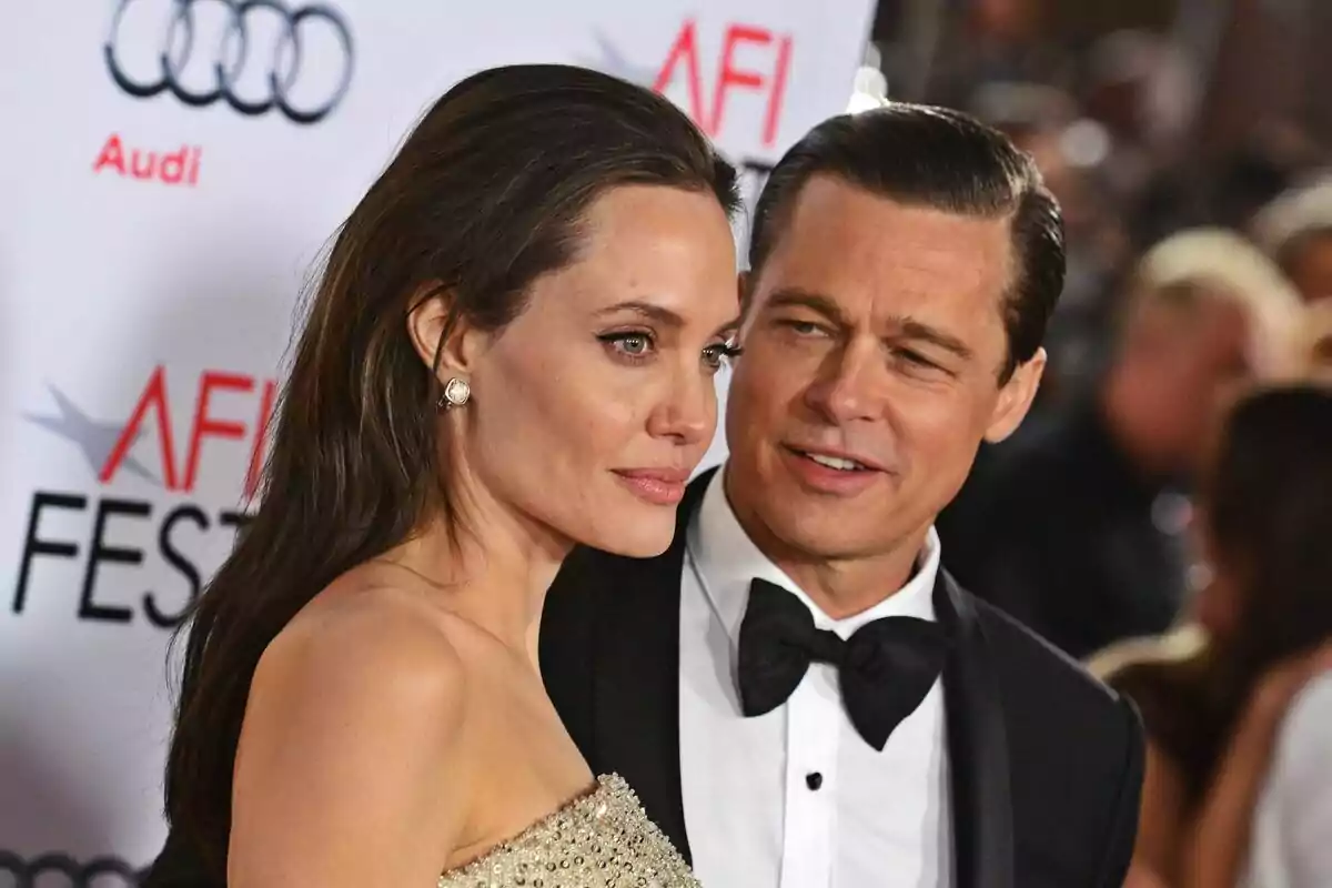 An elegantly dressed couple, consisting of Brad Pitt and Angelina Jolie, poses on a red carpet during a gala event.