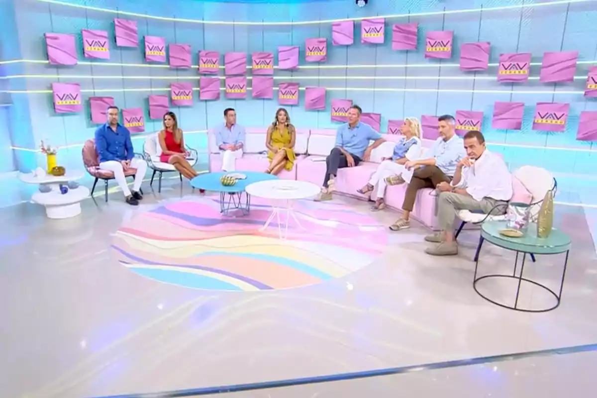 Un grup de persones assegudes en un plató de televisió modern que pertany a 'Vamos a Ver', amb decoració en tons pastel i diversos rètols a la paret. Un grup de persones assegudes en un plató de televisió modern que pertany a 'Vamos a Ver', amb decoració en tons pastel i diversos rètols a la paret.