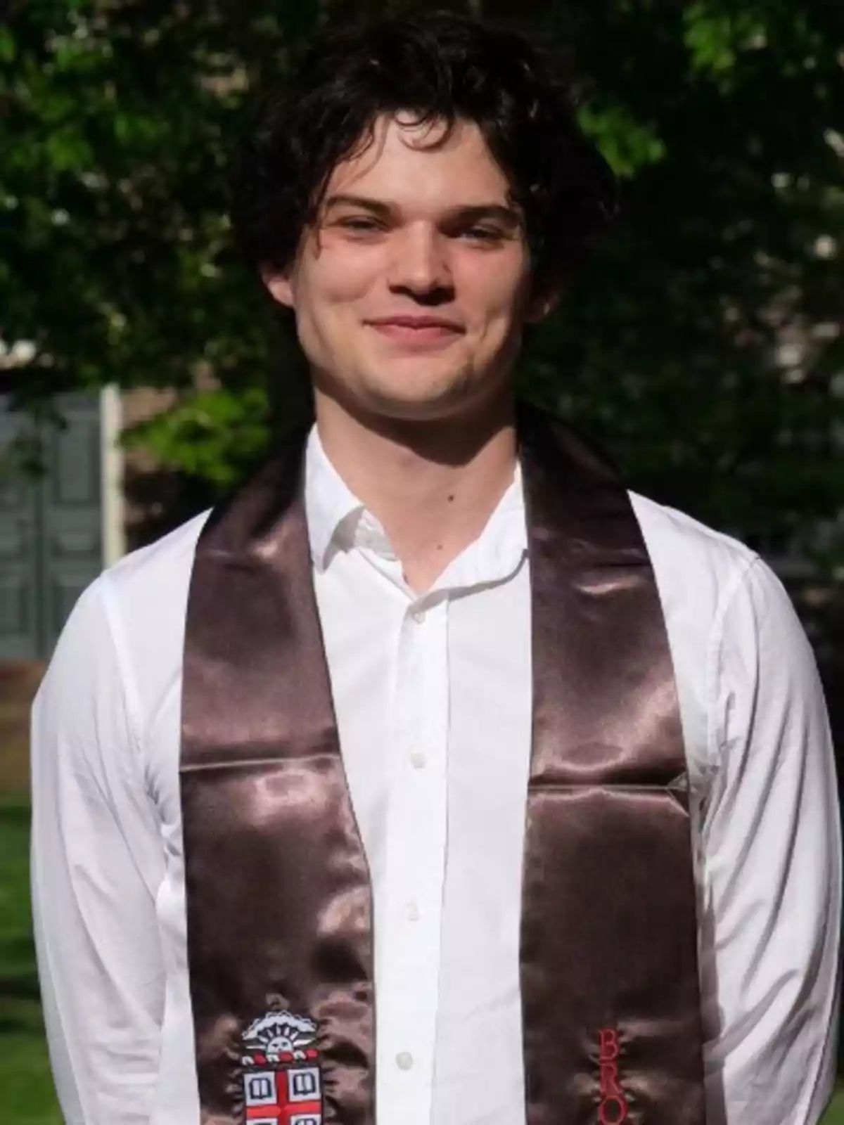 Homer Gere wearing a white jersey and a brown graduation sash posing outdoors