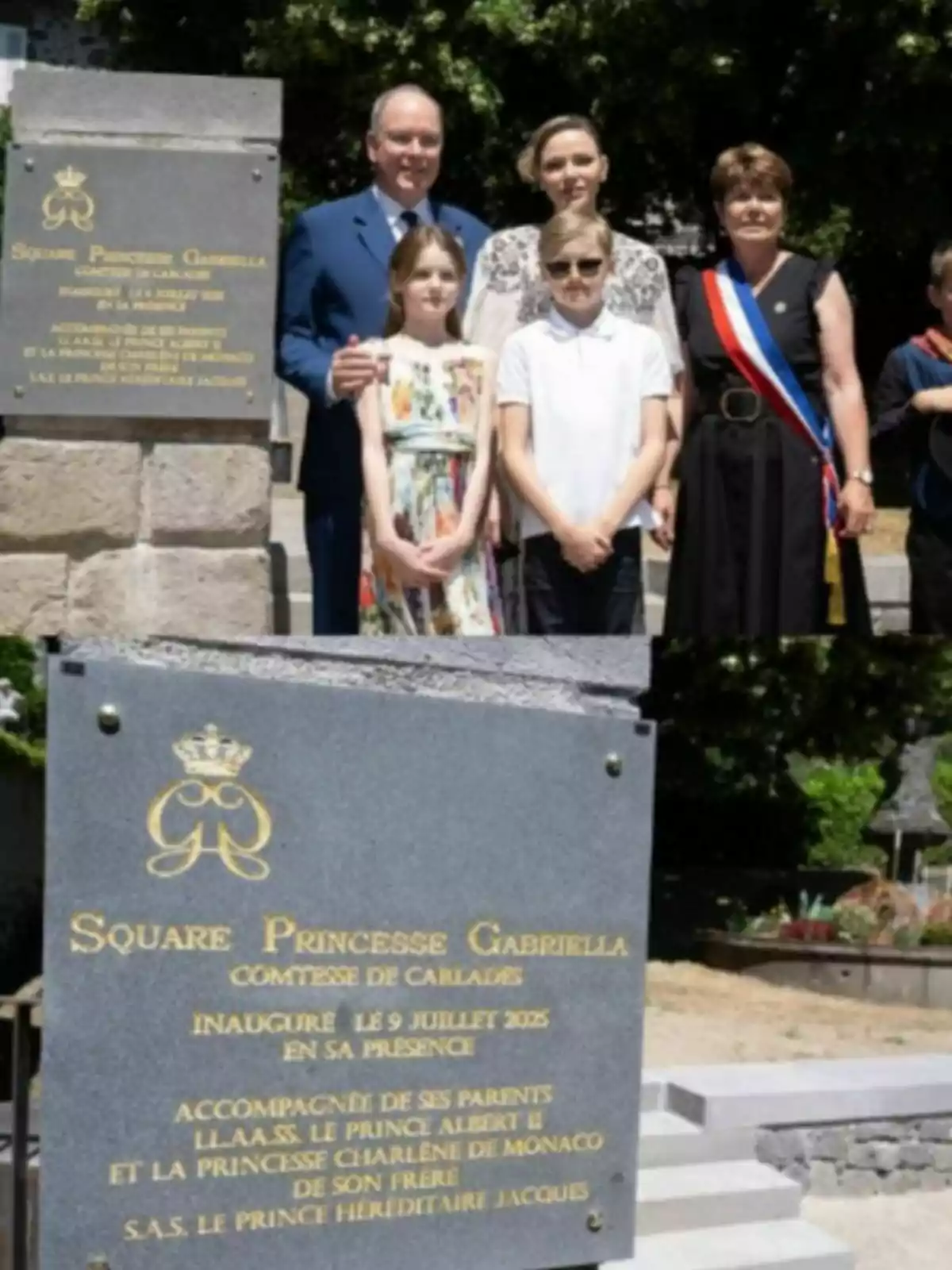 Un grup de persones posa al costat d’una placa commemorativa de pedra grisa amb lletres daurades en un espai a l’aire lliure envoltat d’arbres i jardins. Un grup de persones posa al costat d’una placa commemorativa de pedra grisa amb lletres daurades en un espai a l’aire lliure envoltat d’arbres i jardins.