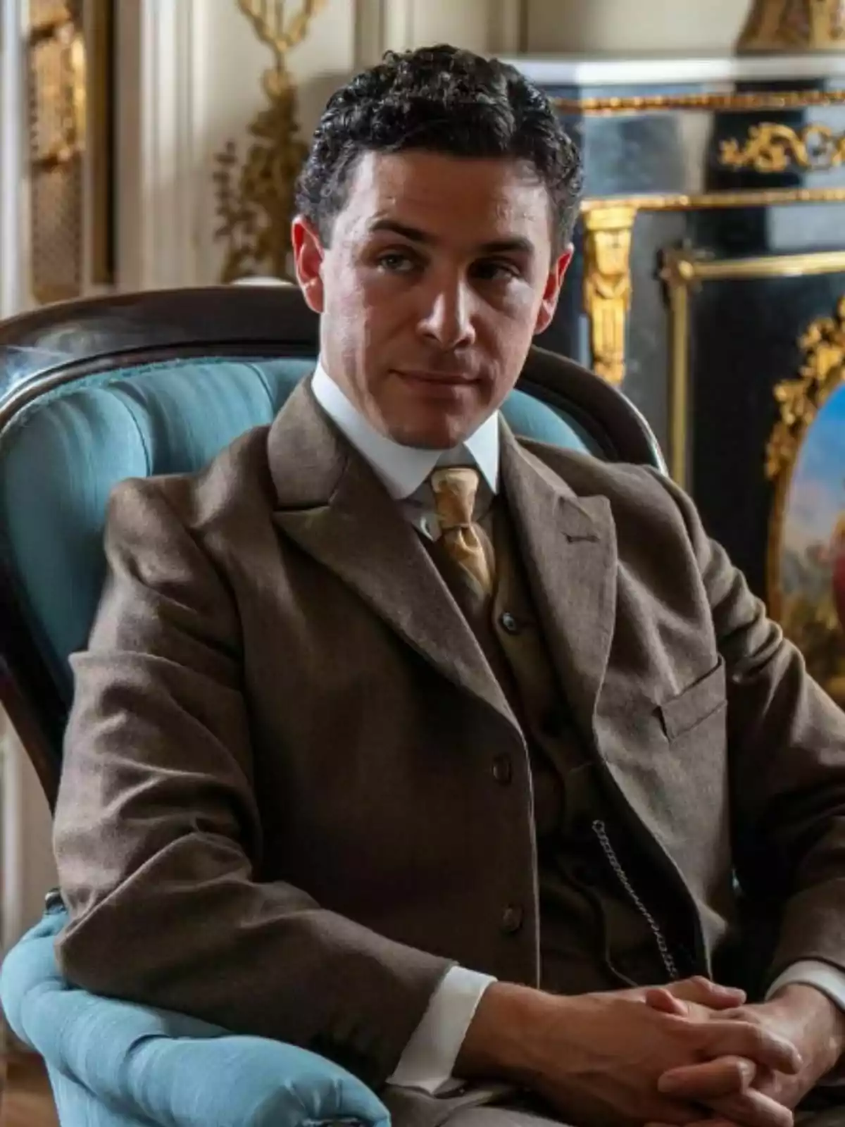 Pepe Nufrio assegut en un sofà blau, vestit amb un vestit marró elegant i corbata beix, en una habitació decorada d’estil clàssic Pepe Nufrio assegut en un sofà blau, vestit amb un vestit marró elegant i corbata beix, en una habitació decorada d’estil clàssic