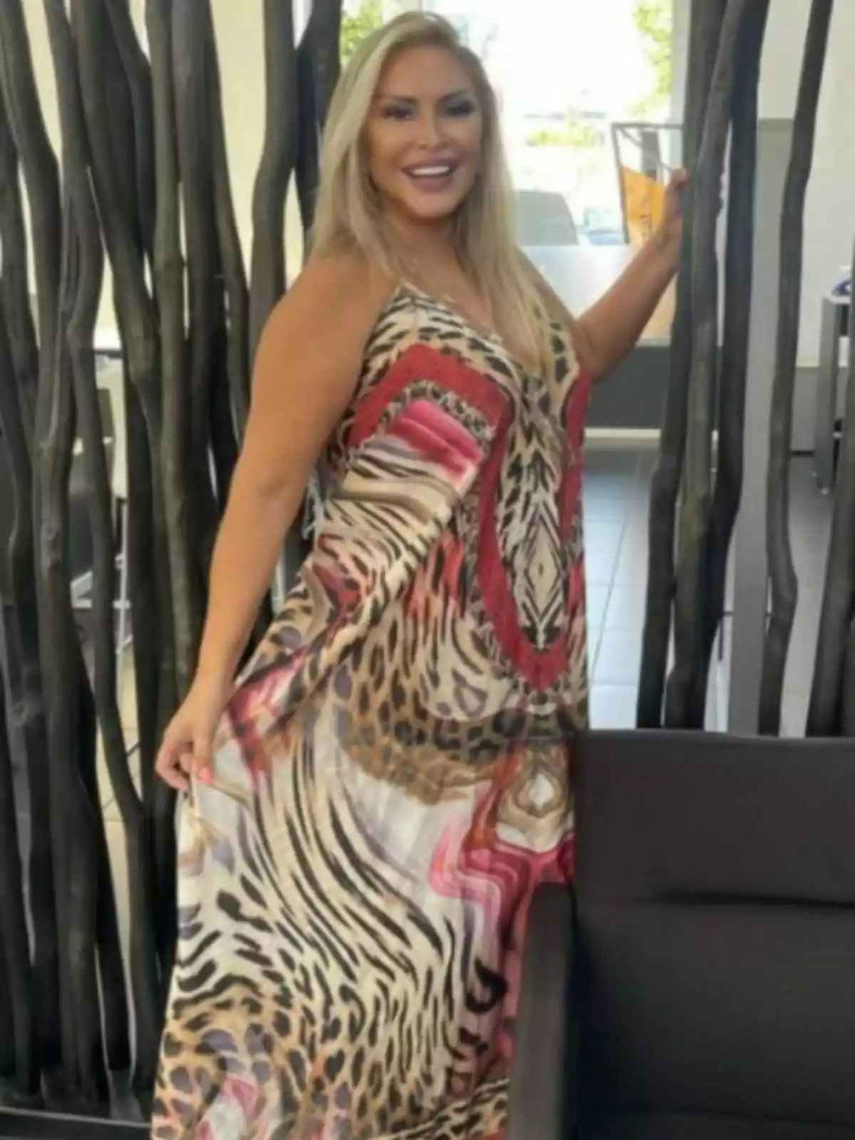 Raquel Mosquera sonriente con vestido largo de estampado animal y detalles en rojo posando junto a una estructura decorativa de madera en un espacio interior moderno Raquel Mosquera sonriente con vestido largo de estampado animal y detalles en rojo posando junto a una estructura decorativa de madera en un espacio interior moderno