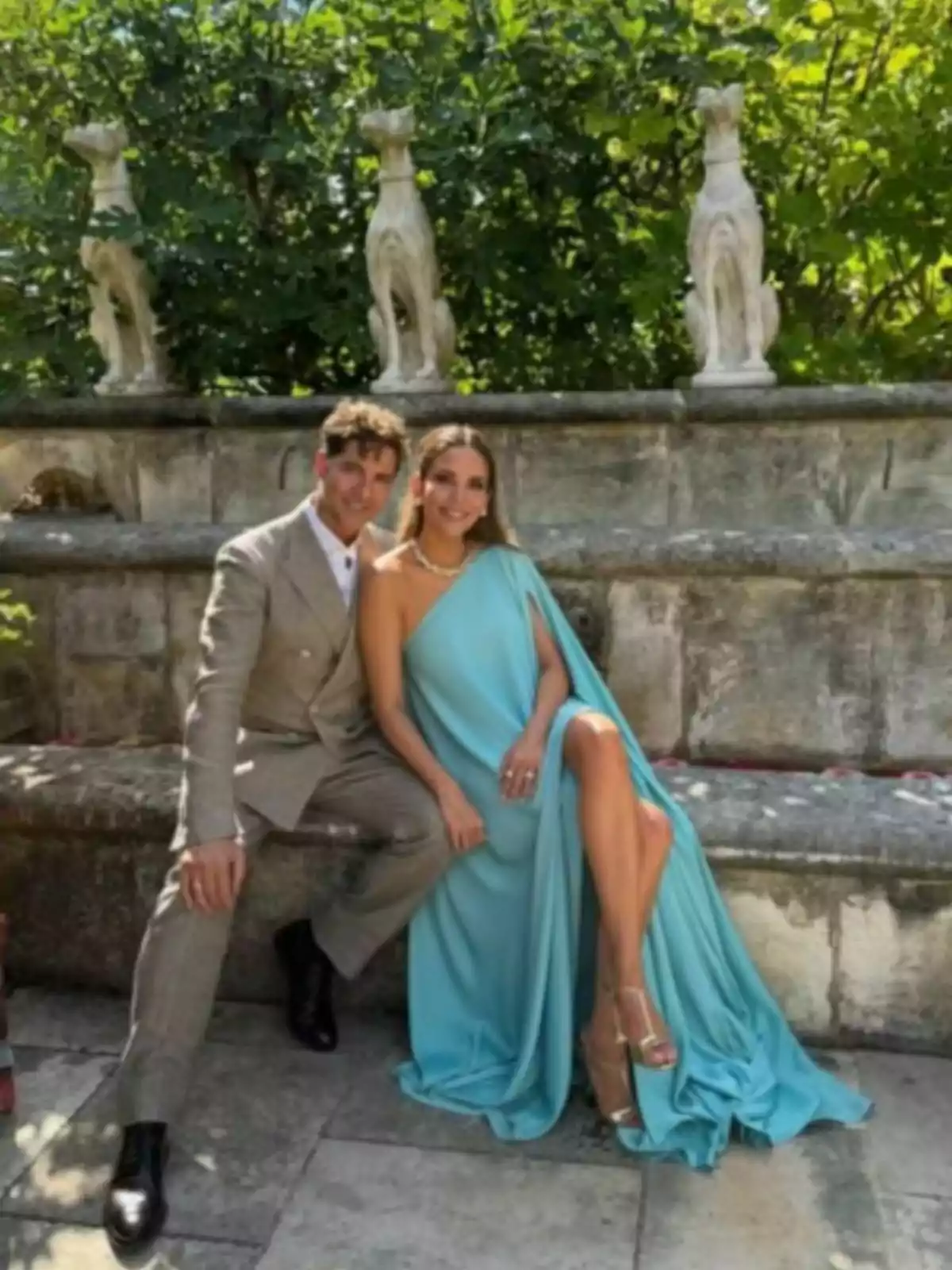 David Bisbal i Rosanna Zanetti elegantament vestida asseguda en un banc de pedra en un jardí amb escultures de gossos al fons David Bisbal i Rosanna Zanetti elegantament vestida asseguda en un banc de pedra en un jardí amb escultures de gossos al fons