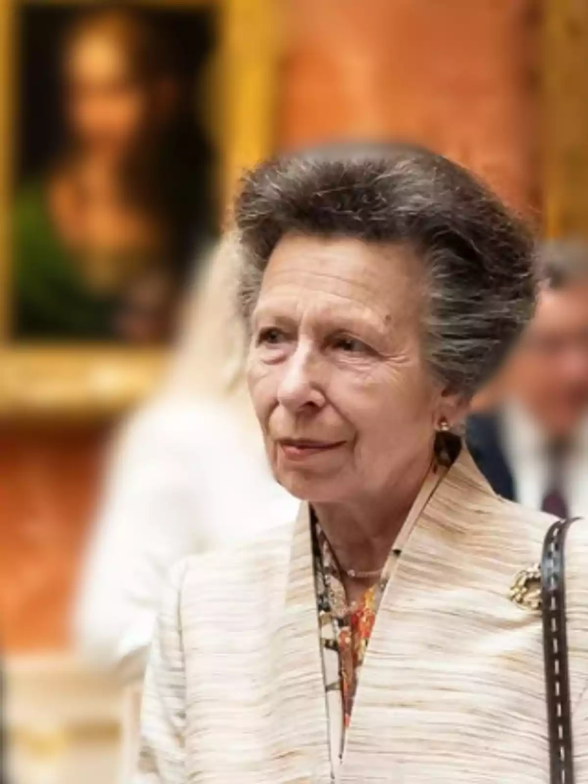 Dona gran de cabells canosos i pentinat voluminós, vestida elegantment amb un fermall daurat, en una galeria d’art amb un quadre desenfocat al fons Dona gran de cabells canosos i pentinat voluminós, vestida elegantment amb un fermall daurat, en una galeria d’art amb un quadre desenfocat al fons