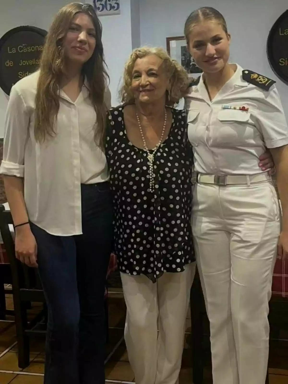 Tres dones posen juntes a l’interior d’un restaurant, una d’elles porta uniforme blanc de gala, una altra porta camisa blanca i pantalons foscos, i la dona del centre porta una brusa de punts i un collaret de perles; dues d’elles són la infanta Sofia i la princesa Leonor. Tres dones posen juntes a l’interior d’un restaurant, una d’elles porta uniforme blanc de gala, una altra porta camisa blanca i pantalons foscos, i la dona del centre porta una brusa de punts i un collaret de perles; dues d’elles són la infanta Sofia i la princesa Leonor.
