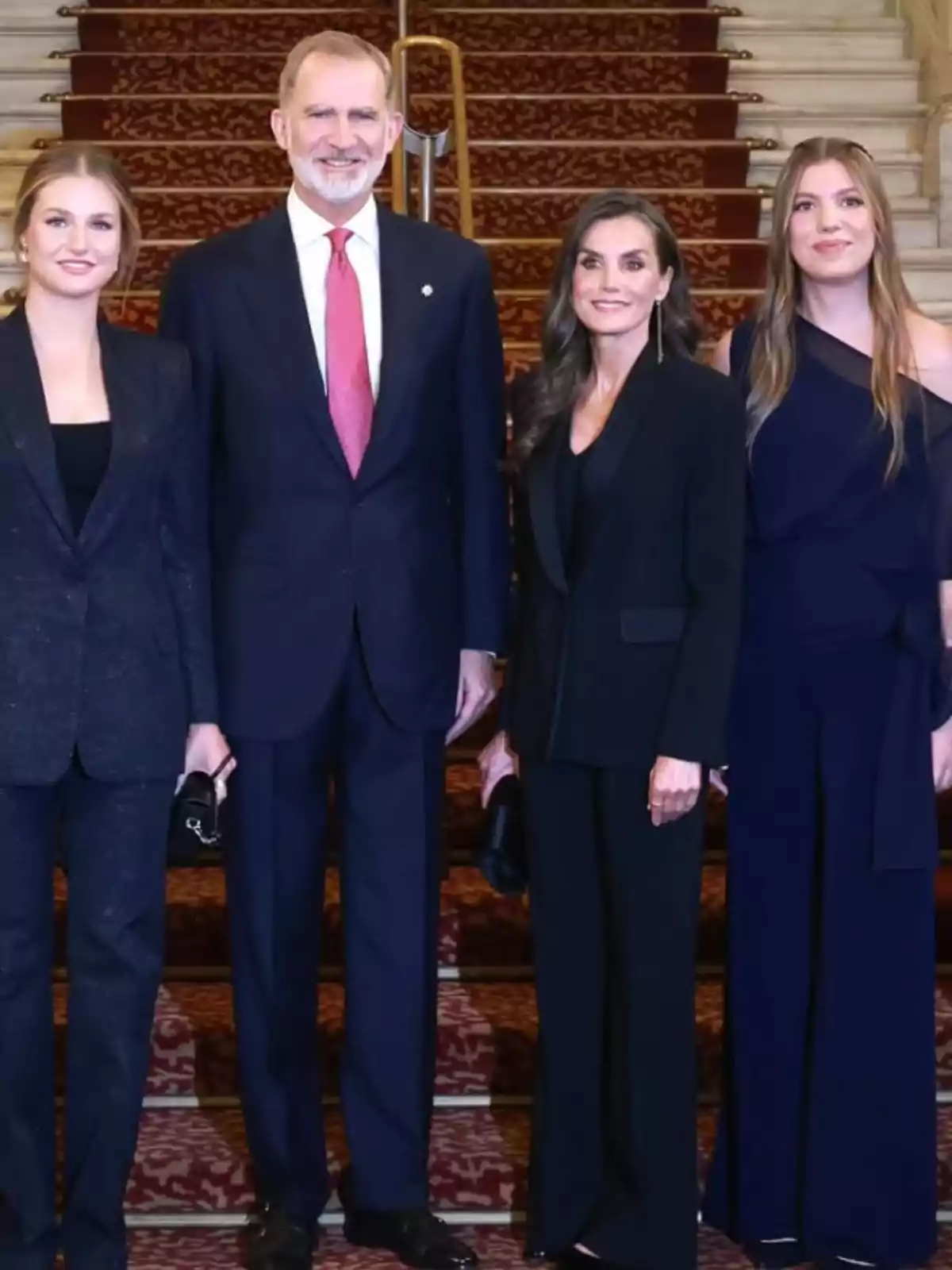 Cuatro personas elegantemente vestidas posan juntas en una escalera alfombrada