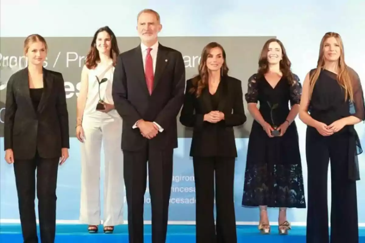 Seis personas posan en un escenario durante una ceremonia de premiación, dos de ellas sostienen trofeos pequeños con forma de planta Seis personas posan en un escenario durante una ceremonia de premiación, dos de ellas sostienen trofeos pequeños con forma de planta