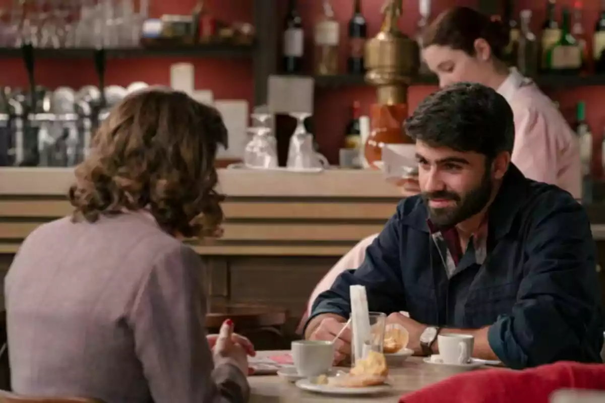 Dues persones conversen en una cafeteria mentre gaudeixen de cafè i rebosteria, al fons una cambrera treballa darrere la barra. Es tracta dels personatges de Raül i Clàudia a 'Sueños de Libertad'. Dues persones conversen en una cafeteria mentre gaudeixen de cafè i rebosteria, al fons una cambrera treballa darrere la barra. Es tracta dels personatges de Raül i Clàudia a 'Sueños de Libertad'.