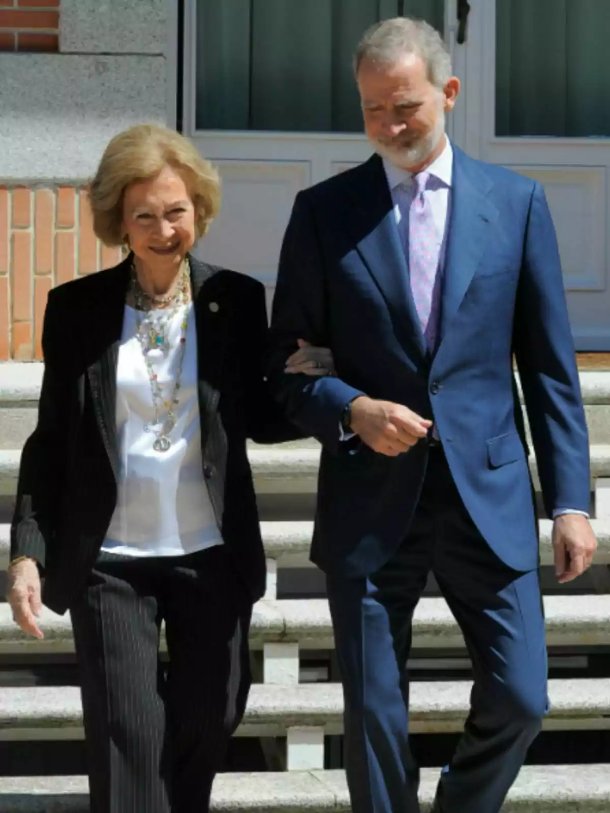 La reina Sofia i Felip VI, elegantment vestits, caminen junts del braç baixant unes escales a l’aire lliure. La reina Sofia i Felip VI, elegantment vestits, caminen junts del braç baixant unes escales a l’aire lliure.