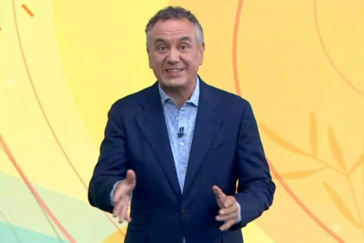 Pla mitjà de Roberto Brasero vestit amb un vestit blau i camisa clara parlant davant d’un fons groc amb línies i formes abstractes. Pla mitjà de Roberto Brasero vestit amb un vestit blau i camisa clara parlant davant d’un fons groc amb línies i formes abstractes.