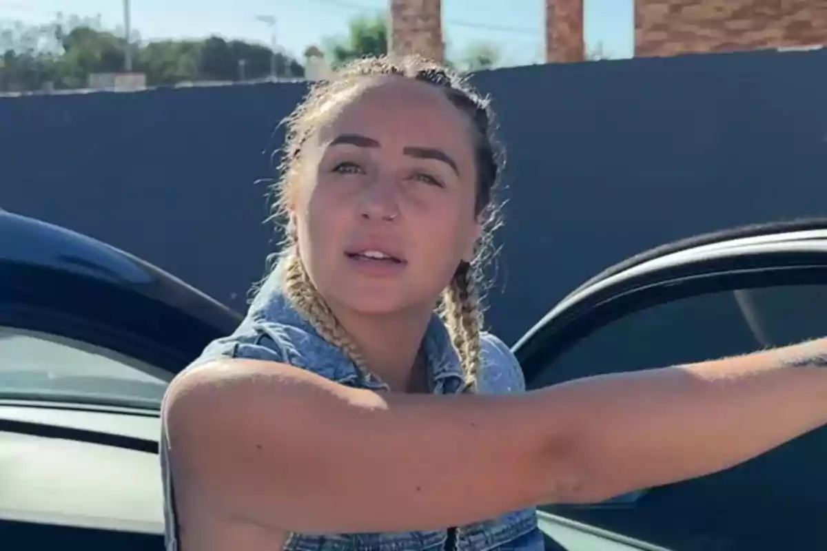 Rocio Flores con trenzas rubias y chaleco de mezclilla junto a un auto negro en un día soleado Rocio Flores con trenzas rubias y chaleco de mezclilla junto a un auto negro en un día soleado