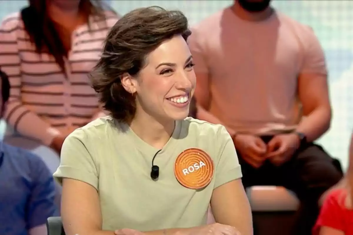 Rosa Rodríguez somrient asseguda en un plató de televisió, que és el de 'Pasapalabra', amb una samarreta clara i un micròfon, porta una xapa amb el nom Rosa i hi ha persones desenfocades al fons. Rosa Rodríguez somrient asseguda en un plató de televisió, que és el de 'Pasapalabra', amb una samarreta clara i un micròfon, porta una xapa amb el nom Rosa i hi ha persones desenfocades al fons.