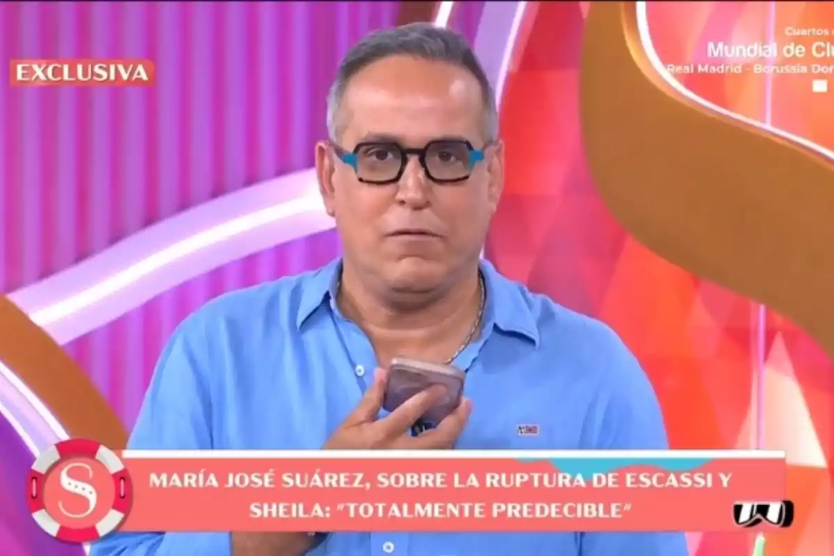 Aurelio Manzano, wearing a blue jersey and glasses, is holding a phone on the set of 'Socialité'. Aurelio Manzano, wearing a blue jersey and glasses, is holding a phone on the set of 'Socialité'.