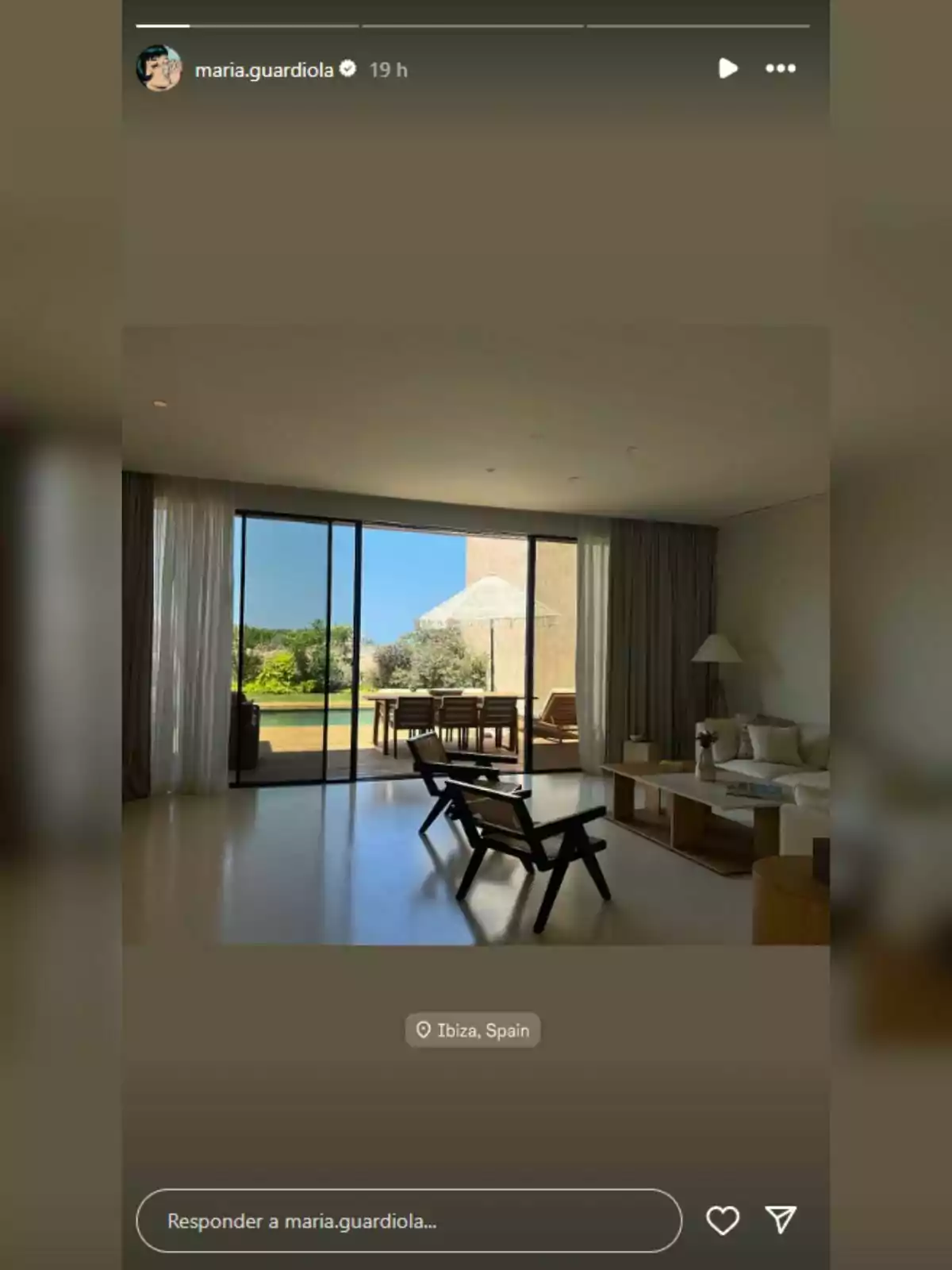 Sala moderna con grandes ventanales que dan a una terraza con mesa y sillas, vista a un jardín y cielo despejado Sala moderna con grandes ventanales que dan a una terraza con mesa y sillas, vista a un jardín y cielo despejado