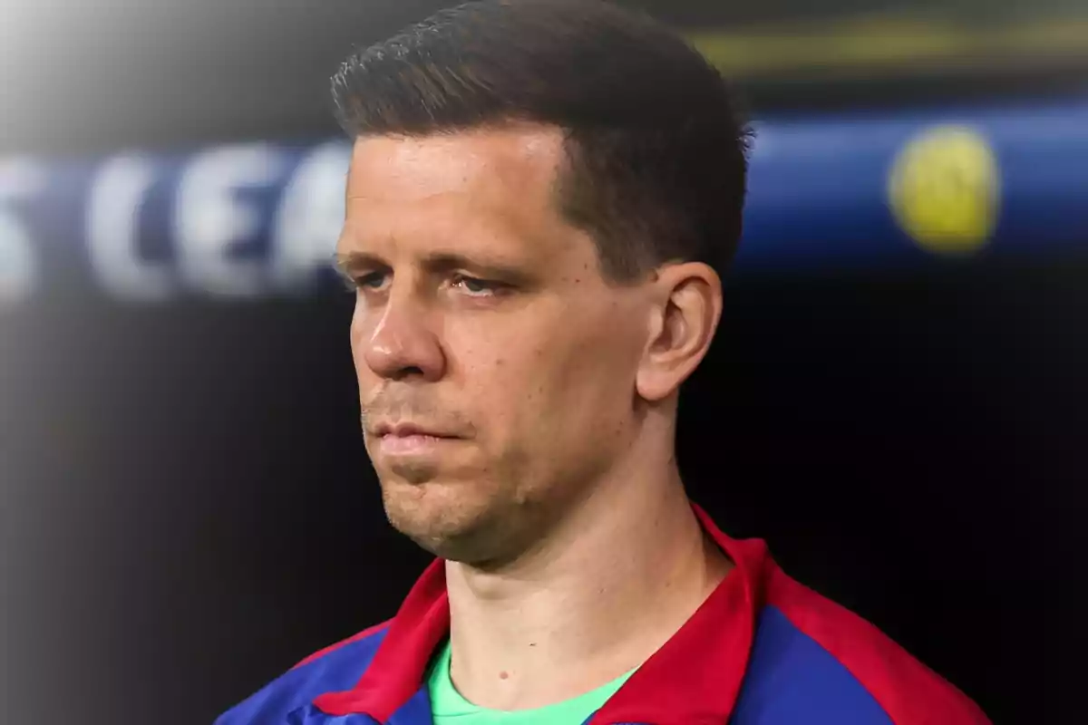 Hombre de cabello corto y expresión seria vistiendo una chaqueta deportiva azul y roja en un entorno deportivo