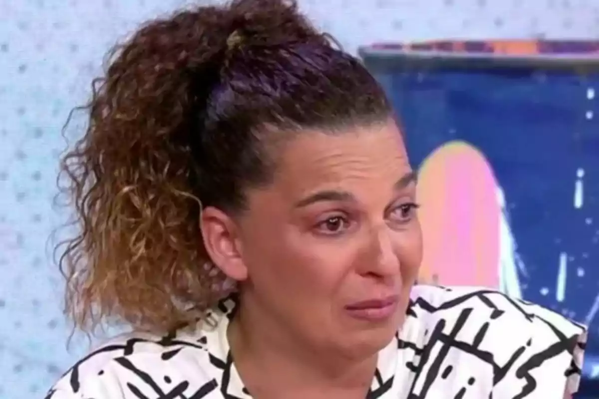 Tamara, hermana de Michu, con el cabello rizado y recogido con expresión de tristeza y ojos llorosos en un set de televisión. Tamara, hermana de Michu, con el cabello rizado y recogido con expresión de tristeza y ojos llorosos en un set de televisión.