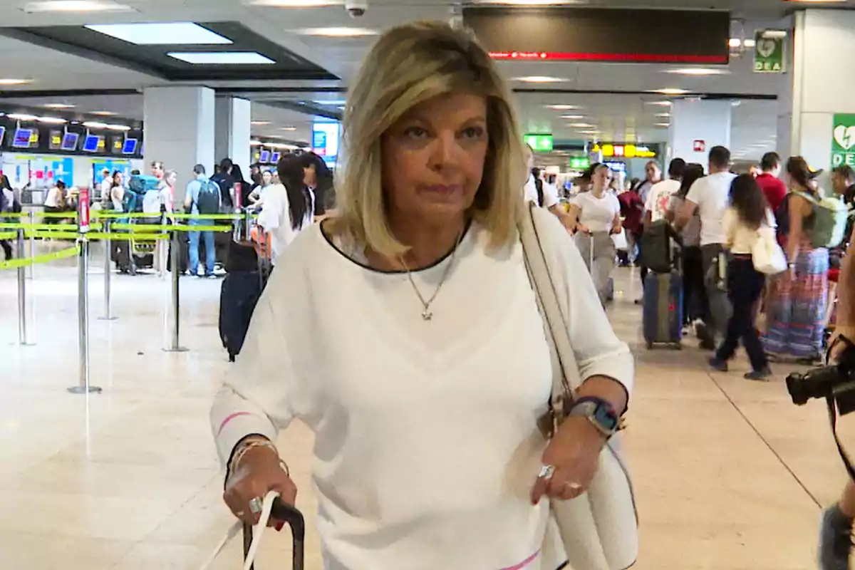 Terelu Campos amb samarreta blanca i bossa caminant amb una maleta en un aeroport ple de gent