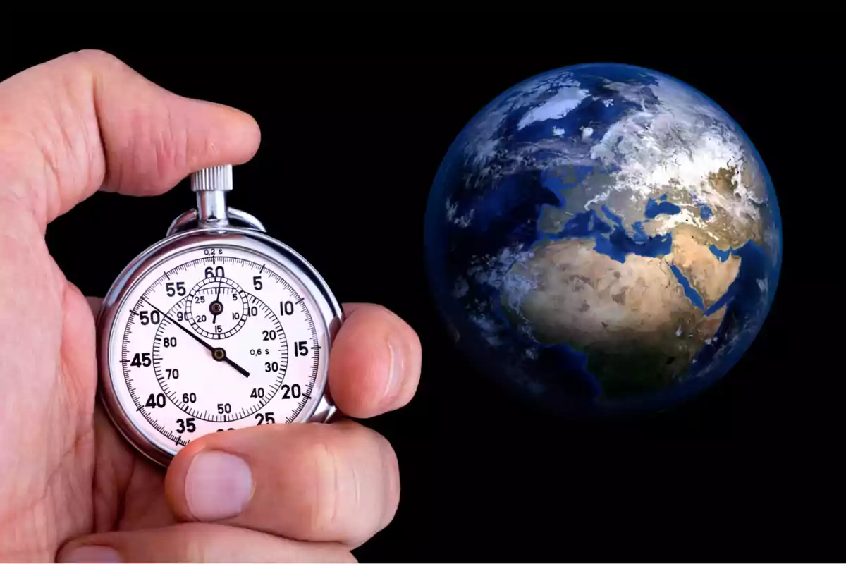 Mano sosteniendo un cronómetro plateado frente a una imagen del planeta Tierra sobre fondo negro Mano sosteniendo un cronómetro plateado frente a una imagen del planeta Tierra sobre fondo negro