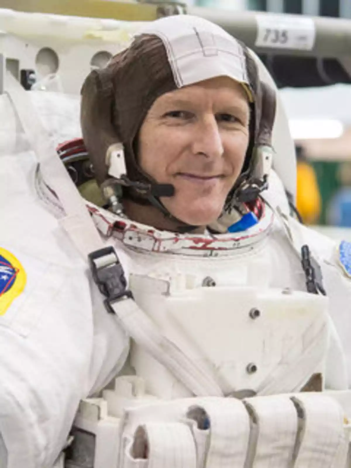 Tim Peake con casco marrón y traje espacial blanco sonriendo mientras se prepara para una misión Tim Peake con casco marrón y traje espacial blanco sonriendo mientras se prepara para una misión