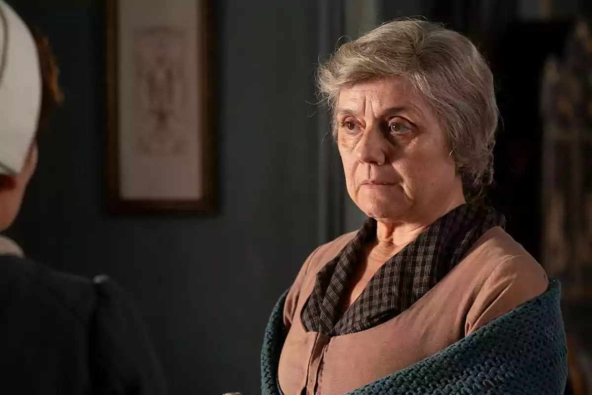 Raimunda amb expressió seriosa embolicada en un xal blau dins d’una habitació antiga. Captura de ‘Valle Salvaje’ Raimunda amb expressió seriosa embolicada en un xal blau dins d’una habitació antiga. Captura de ‘Valle Salvaje’
