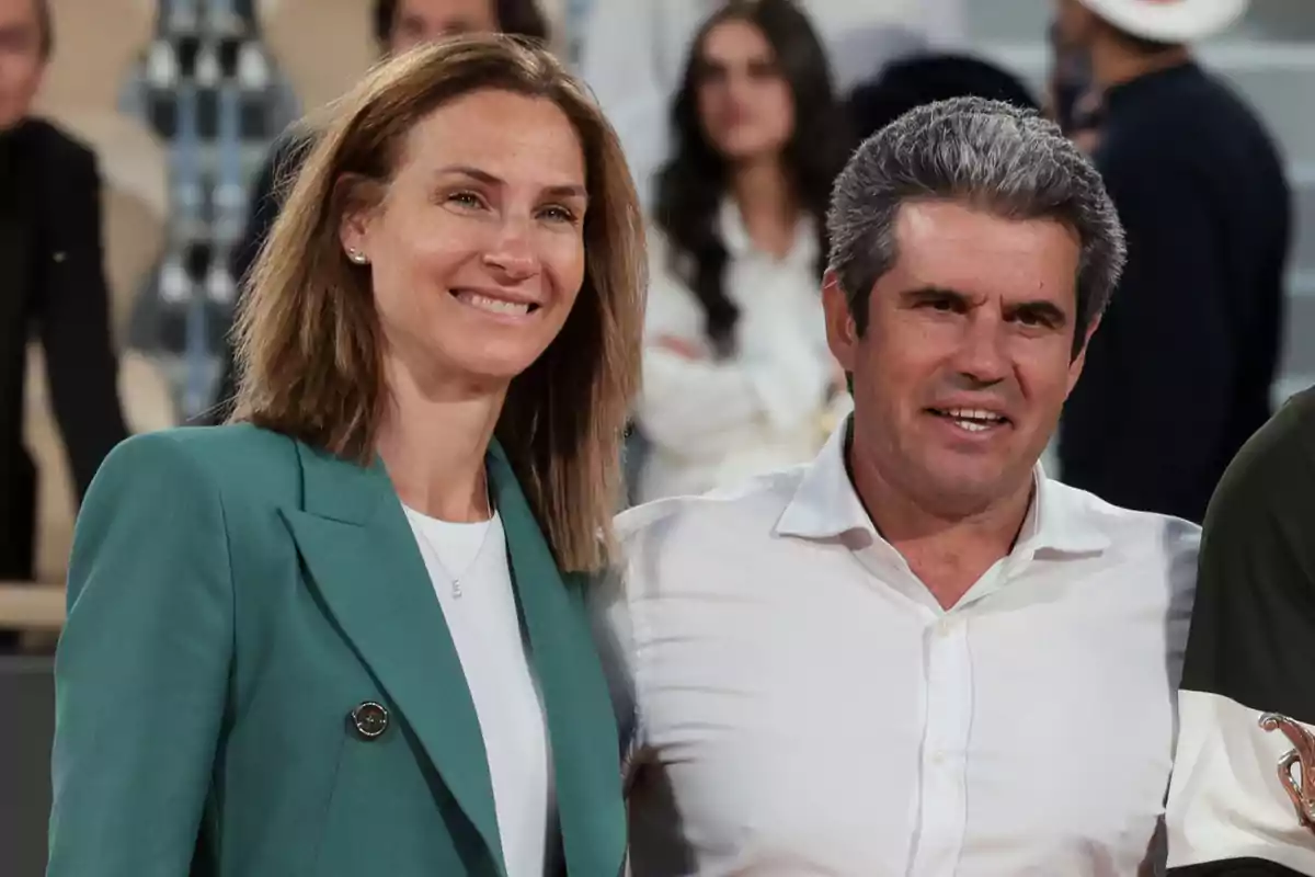 Virginia Garfia amb jaqueta verda i Carlos Alcaraz González amb camisa blanca posen junts i somriuen en un esdeveniment social amb persones al fons. Virginia Garfia amb jaqueta verda i Carlos Alcaraz González amb camisa blanca posen junts i somriuen en un esdeveniment social amb persones al fons.