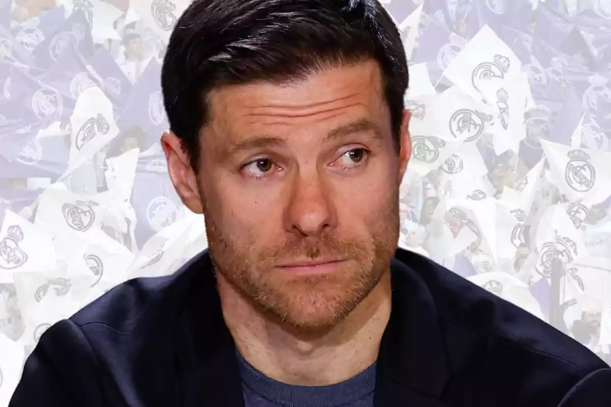 Hombre de cabello corto y barba mirando hacia un lado con banderas blancas y moradas de un equipo de fútbol al fondo Hombre de cabello corto y barba mirando hacia un lado con banderas blancas y moradas de un equipo de fútbol al fondo