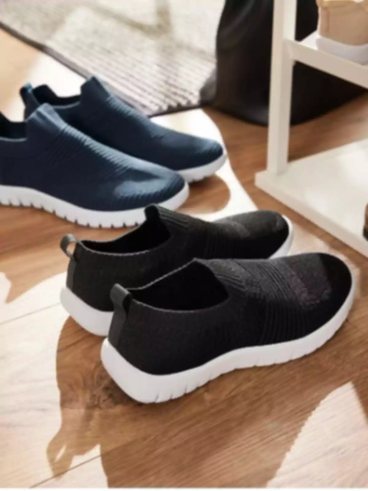 Dos parells de vambes esportives sense cordons de color negre i blau marí amb sola blanca sobre un terra de fusta Dos parells de vambes esportives sense cordons de color negre i blau marí amb sola blanca sobre un terra de fusta