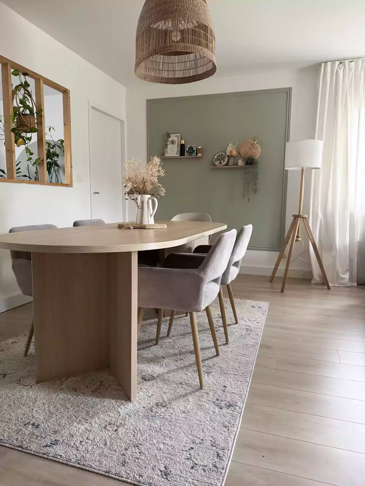 Comedor moderno y acogedor con mesa de madera clara, sillas tapizadas en gris, alfombra beige, lámpara de mimbre, pared verde decorada y luz natural entrando por una ventana con cortinas blancas. Comedor moderno y acogedor con mesa de madera clara, sillas tapizadas en gris, alfombra beige, lámpara de mimbre, pared verde decorada y luz natural entrando por una ventana con cortinas blancas.