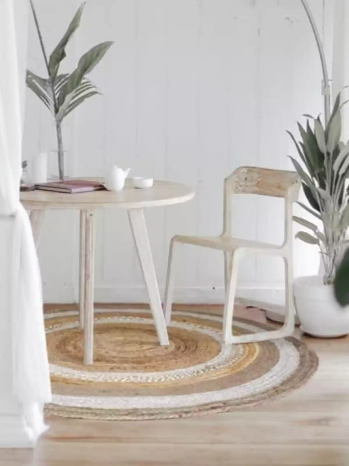 Espai interior minimalista amb taula rodona de fusta clara, cadira a joc, catifa circular de teixit i plantes decoratives Espai interior minimalista amb taula rodona de fusta clara, cadira a joc, catifa circular de teixit i plantes decoratives