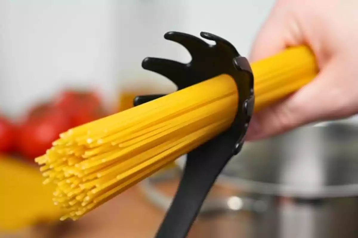 Una mano sostiene espaguetis crudos con una cuchara para pasta sobre una olla en la cocina Una mano sostiene espaguetis crudos con una cuchara para pasta sobre una olla en la cocina