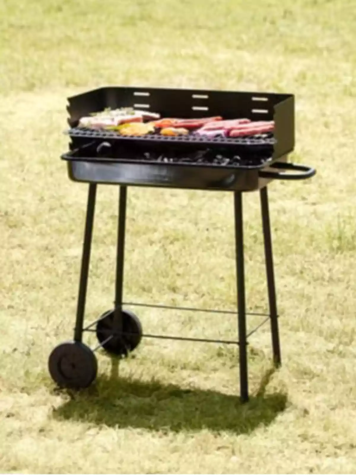 Barbacoa de carbó portàtil amb rodes en un jardí rostint carn i verdures Barbacoa de carbó portàtil amb rodes en un jardí rostint carn i verdures