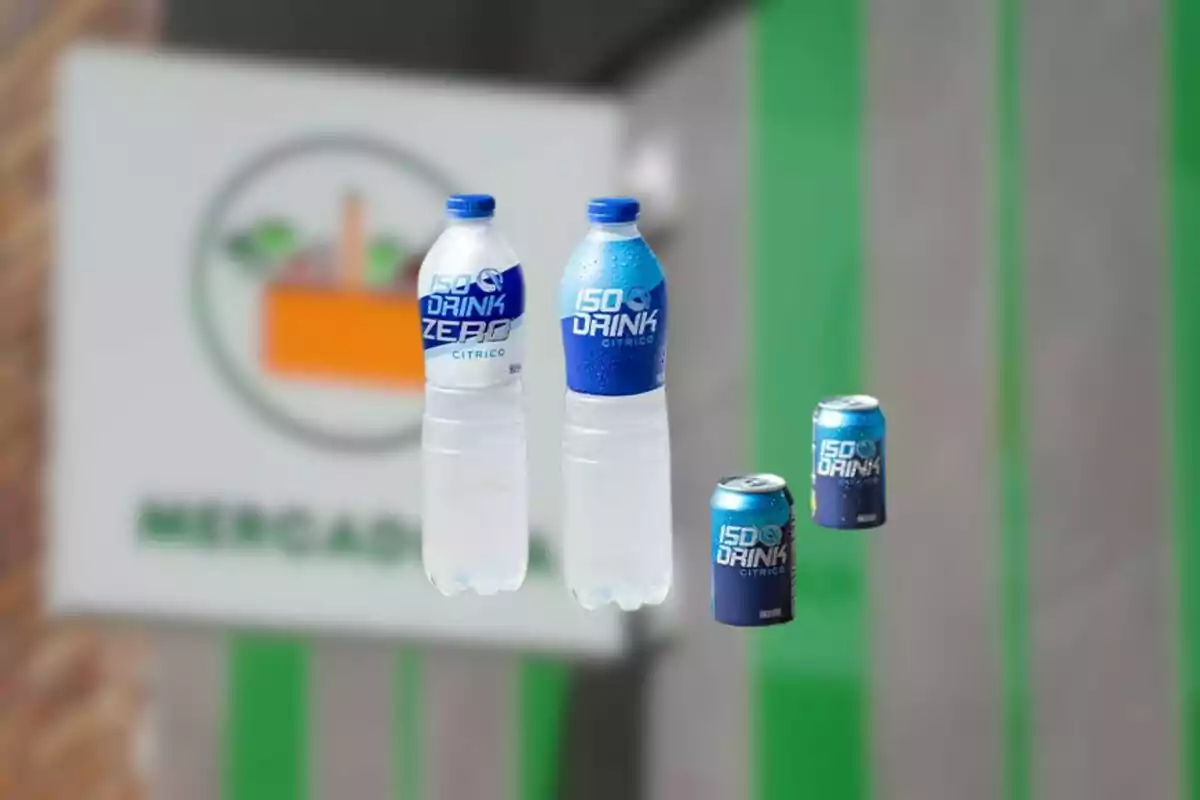 Cuatro bebidas isotónicas en envases de botella y lata con etiquetas azules y fondo desenfocado de un supermercado