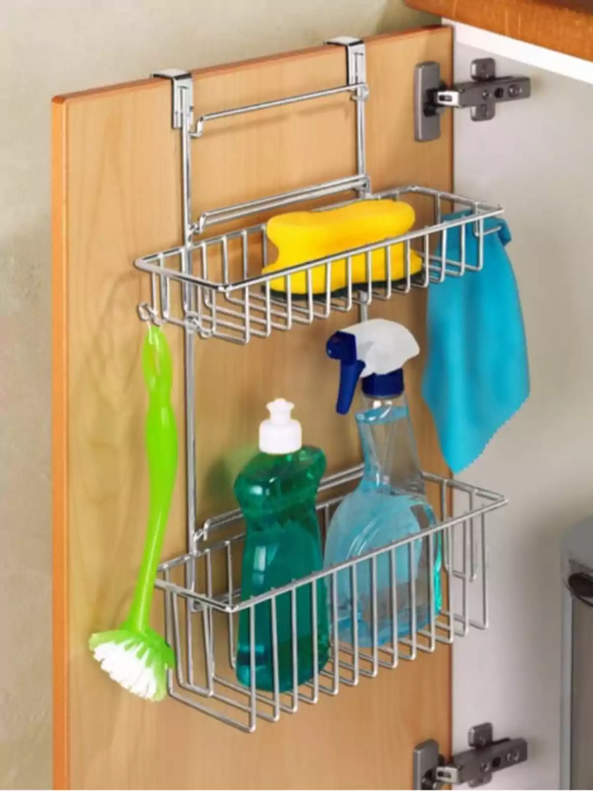 Organitzador metàl·lic penjat a la porta d’un armari de cuina amb una esponja groga, un drap blau, un raspall verd, una ampolla de detergent i un polvoritzador de neteja. Organitzador metàl·lic penjat a la porta d’un armari de cuina amb una esponja groga, un drap blau, un raspall verd, una ampolla de detergent i un polvoritzador de neteja.