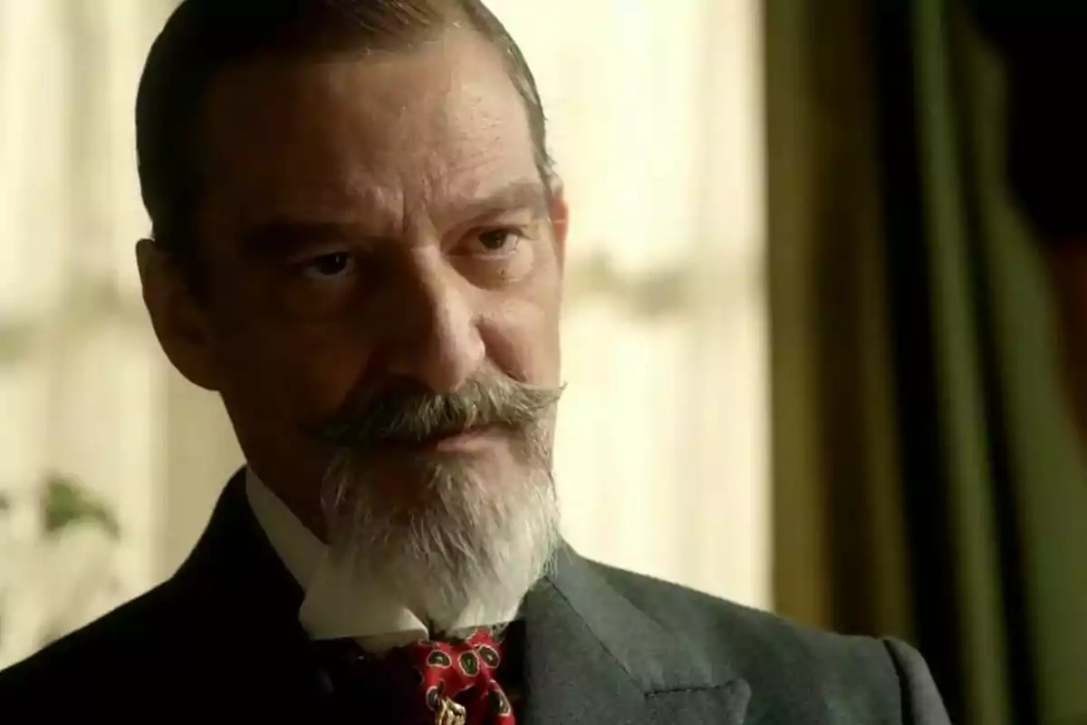 Alfonso Mendiguchía amb bigoti i barba canosa vestit amb un vestit fosc i corbata vermella mirant amb una expressió seriosa. Alfonso Mendiguchía amb bigoti i barba canosa vestit amb un vestit fosc i corbata vermella mirant amb una expressió seriosa.