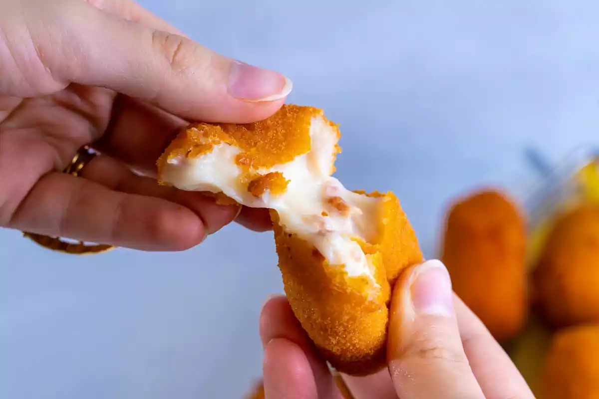 Manos partiendo una croqueta dorada con relleno cremoso de bechamel Manos partiendo una croqueta dorada con relleno cremoso de bechamel