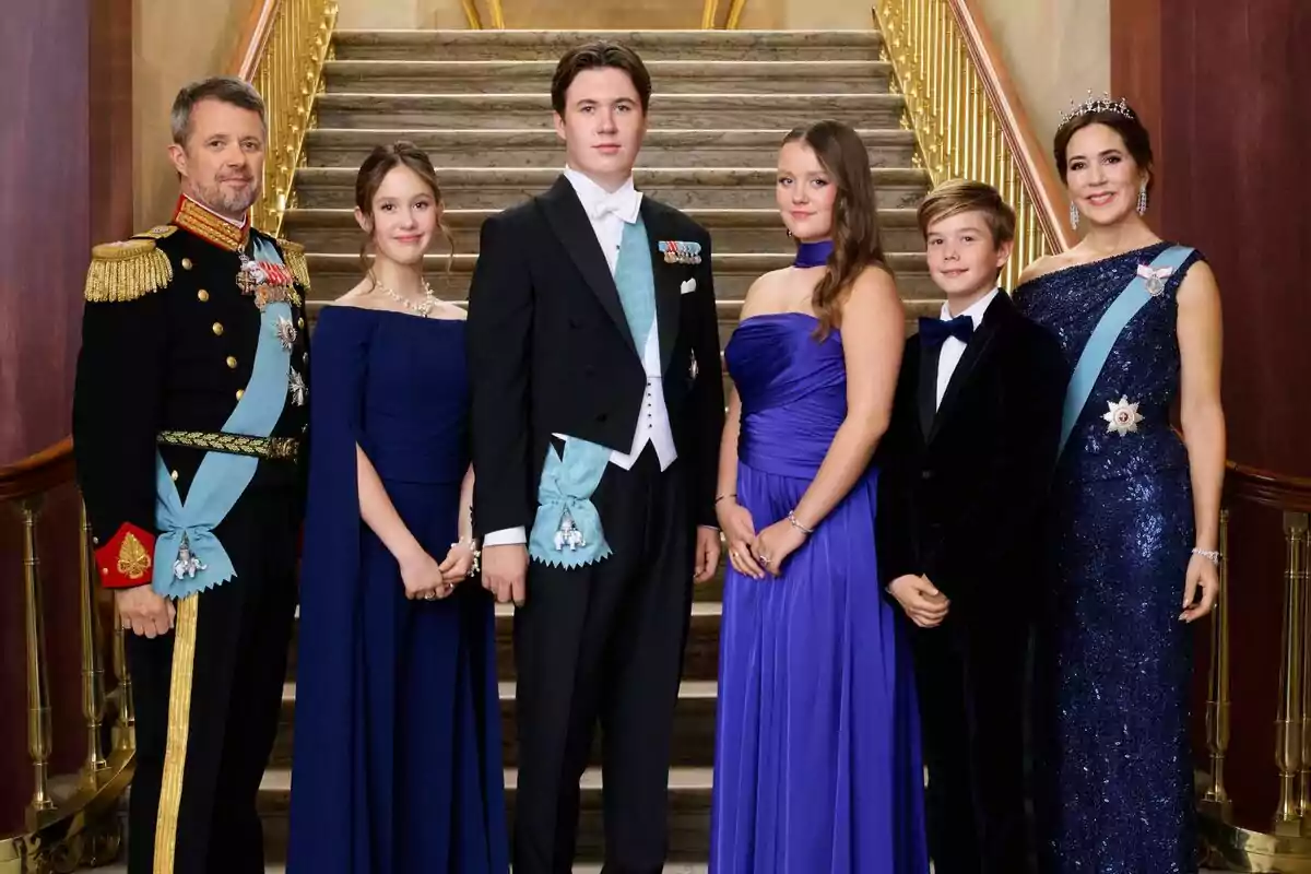 Frederic, Josefina, Christian, Isabel, Vicent i María de Dinamarca elegantment vestits posen en una escala de marbre amb baranes daurades, algunes porten bandes i medalles, i una dona porta una tiara. Frederic, Josefina, Christian, Isabel, Vicent i María de Dinamarca elegantment vestits posen en una escala de marbre amb baranes daurades, algunes porten bandes i medalles, i una dona porta una tiara.