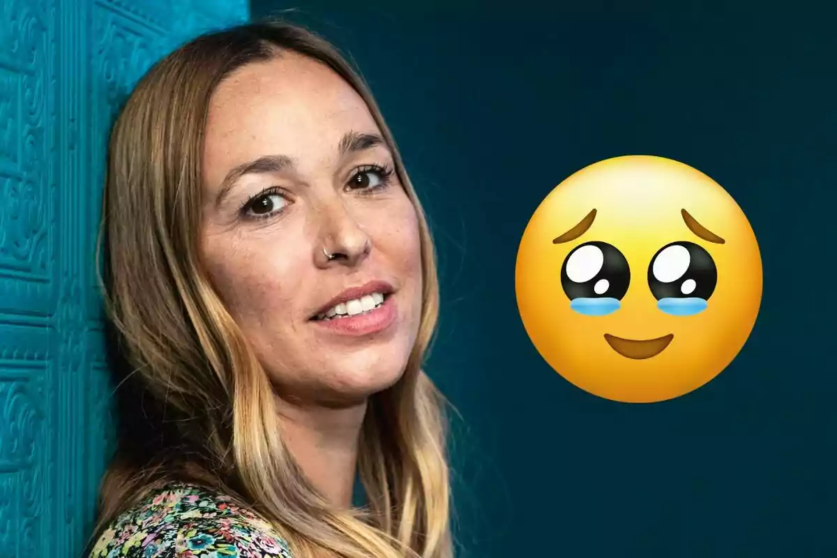 Mujer de cabello largo y rubio apoyada en una pared azul con un emoji de carita con lágrimas y expresión tierna a su lado